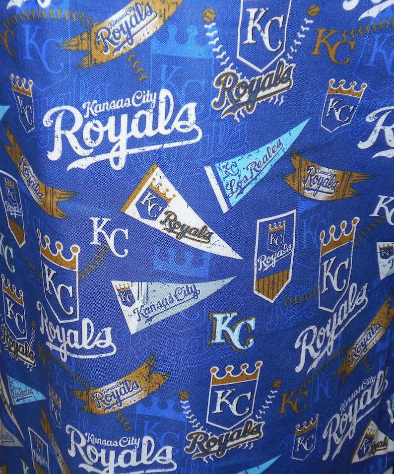 May include: A blue fabric with a repeating pattern of the Kansas City Royals logo. The logo features a crown, the letters "KC", and the word "Royals".
