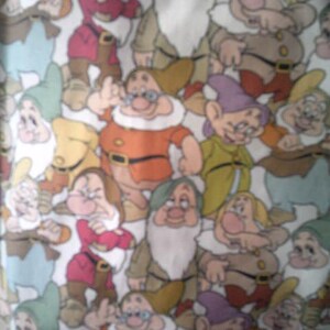 May include: Fabric featuring a repeating pattern of cartoon dwarfs in various poses. The dwarfs are depicted in a variety of colors, including red, green, yellow, and brown, with white beards and hats. The background is a light cream color.
