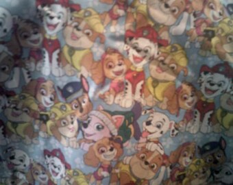 May include: A light blue fabric featuring a repeating pattern of cartoon puppies from the Paw Patrol series. The puppies are depicted in various poses and outfits, with a variety of colors including brown, yellow, red, and white.