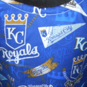 May include: Blue fabric with a repeating pattern of the Kansas City Royals logo. The logo features a crown, the letters "KC", and the word "Royals".