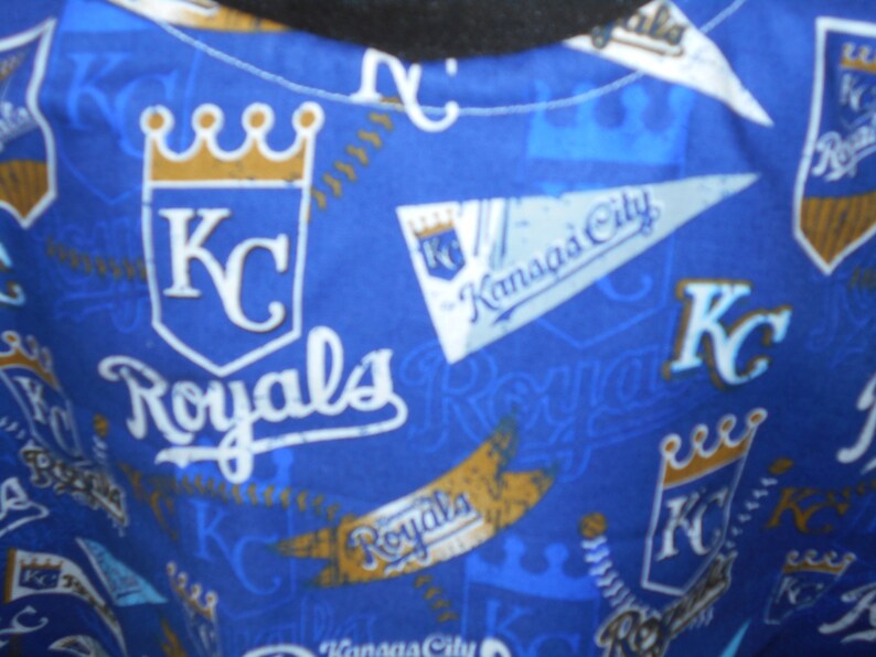 May include: Blue fabric with a repeating pattern of the Kansas City Royals logo. The logo features a crown, the letters "KC", and the word "Royals".