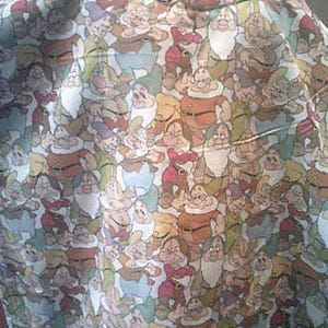 May include: A fabric with a repeating pattern of cartoon dwarfs in various poses. The dwarfs are depicted with white beards, colorful outfits, and expressive faces. The color palette includes shades of brown, red, green, and blue.