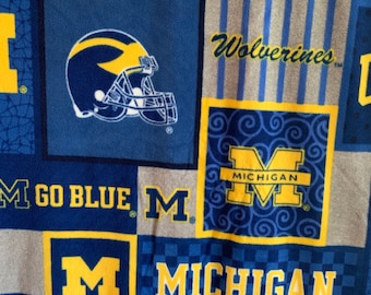 May include: A blue and yellow fleece blanket with the University of Michigan logo and the words "Go Blue" and "Wolverines".