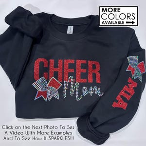 May include: Black sweatshirt with red glitter lettering that says "CHEER Mom" and a red glitter bow with rhinestones on the left side. The right sleeve has a red glitter bow with rhinestones and the word "MIA" in red glitter.
