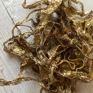 May include: A tangled pile of gold metallic ribbon. The ribbon has a woven, mesh-like texture and reflects light, creating a shimmering effect. The ribbon is likely used for crafts, gift wrapping, or decorative purposes.