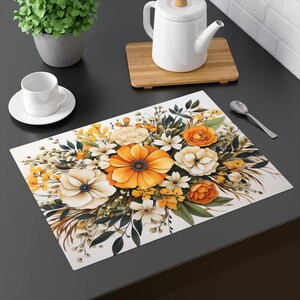 May include: A white placemat with a floral design featuring orange, white, and yellow flowers. The flowers are arranged in a bouquet and have green leaves.
