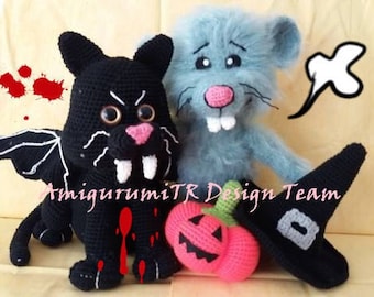 May include: A selection of handmade crochet Halloween decorations. Features a black bat with white fangs and wings, a blue mouse, a pink pumpkin, and a black witch hat. The text "AmigurumiTR Design Team" is visible.