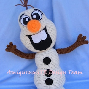 May include: A crocheted Olaf snowman toy from the movie Frozen. Olaf is white with a brown crocheted hair, black eyes, an orange nose, and a black mouth. He has two black buttons on his body and brown crocheted arms.
