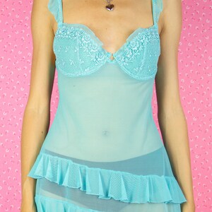 The Vintage Y2K Blue Mesh Mini Dress is a pastel blue semi-sheer mesh babydoll featuring ruffles, adjustable straps adorned with rhinestones, floral details, and a cut-out back with a bow, presenting a super sexy lingerie nightgown from the 2000s.