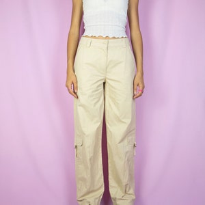 The Y2K Beige Cargo Pants are vintage mid-rise wide pants with pockets and a front zipper closure. Cyber grunge 2000s utility trousers.