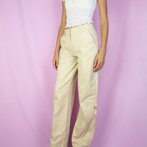 The Y2K Beige Cargo Pants are vintage mid-rise wide pants with pockets and a front zipper closure. Cyber grunge 2000s utility trousers.