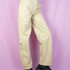 The Y2K Beige Cargo Pants are vintage mid-rise wide pants with pockets and a front zipper closure. Cyber grunge 2000s utility trousers.