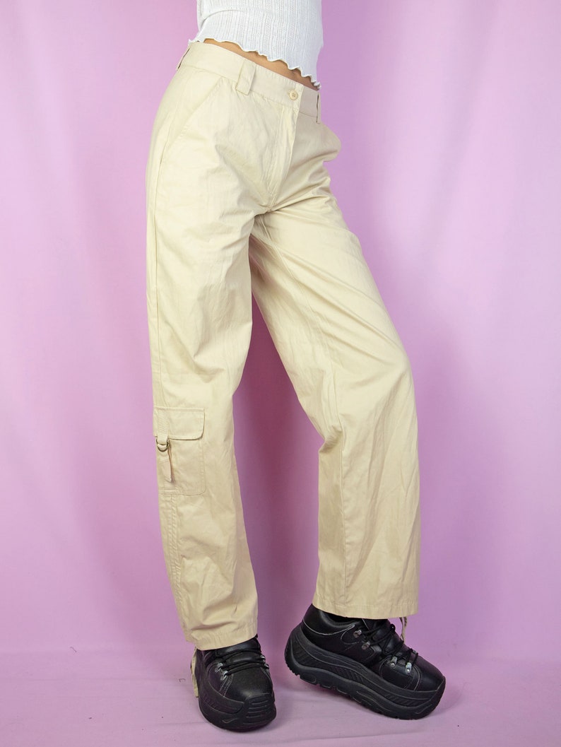 The Y2K Beige Cargo Pants are vintage mid-rise wide pants with pockets and a front zipper closure. Cyber grunge 2000s utility trousers.