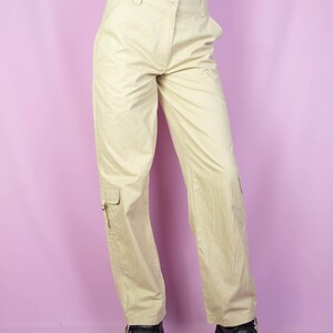 The Y2K Beige Cargo Pants are vintage mid-rise wide pants with pockets and a front zipper closure. Cyber grunge 2000s utility trousers.