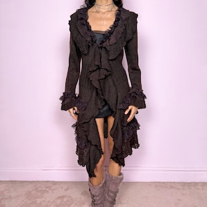 以下が含まれることがあります： フリルとレースのアクセントが施された、長くて濃い茶色のニットカーディガン。カーディガンは長袖で、非対称の裾が特徴です。デザインには、ハイカラーと袖口の装飾的なフリルが含まれています。