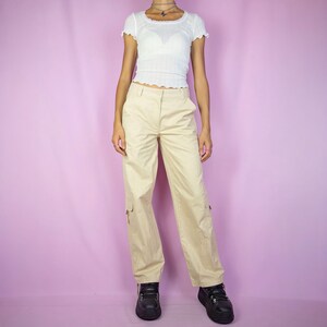 The Y2K Beige Cargo Pants are vintage mid-rise wide pants with pockets and a front zipper closure. Cyber grunge 2000s utility trousers.