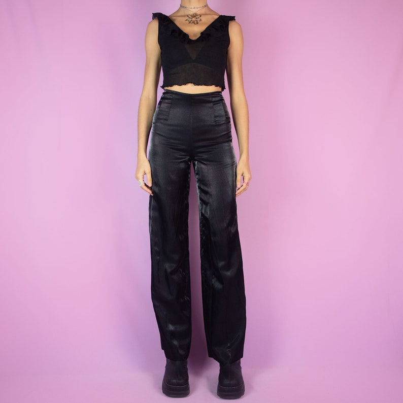 The Vintage 90s Black Tailored Wide Pants are shiny black iridescent pants with high-rise pleats, featuring a side zipper closure and wide legs. Elegant evening party 1990s classic pleated trousers.