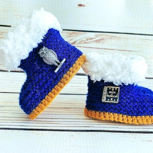 May include: A pair of handmade baby booties. The booties are blue with white faux fur trim and a gold-colored sole. One bootie has an owl pin, and the other has a pin that says "Book of Spells".