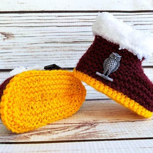 May include: Crocheted baby booties and matching taco-shaped item. The booties are burgundy with a yellow trim and white faux fur trim. A silver owl pin adorns the side. The taco-shaped item is yellow with burgundy trim.