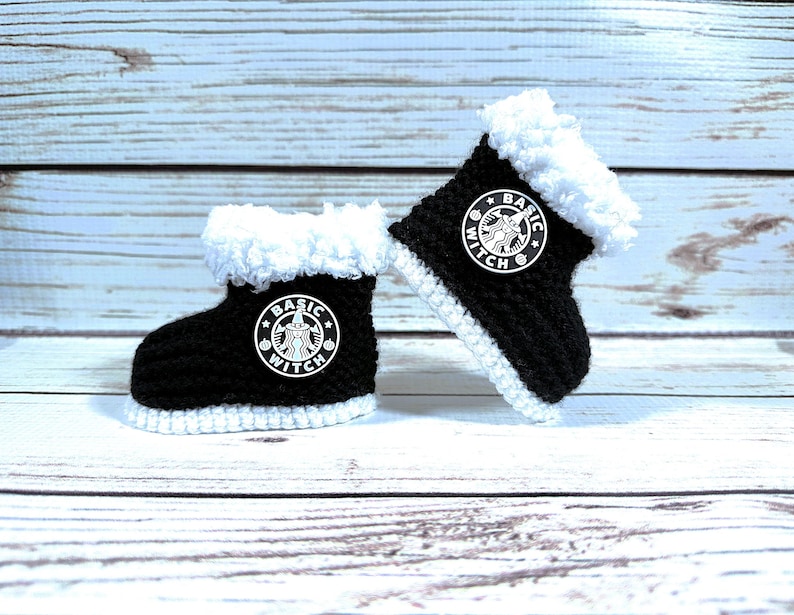 May include: A pair of black and white crocheted baby boots. The boots have a white fluffy trim and a white stitched sole. Each boot features a white circular logo with the words "Basic Witch".