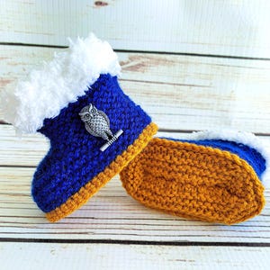 May include: A pair of handmade crochet baby booties. The booties are blue with a white fluffy trim and a silver owl embellishment. The soles are mustard yellow. A cozy and unique baby gift.