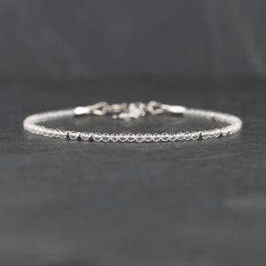 May include: A delicate bracelet featuring a single strand of small, clear, faceted beads interspersed with tiny, polished silver-toned metal spacers. The bracelet includes a silver-toned metal lobster claw clasp and an adjustable chain link extension.