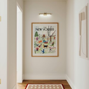 May include: A hallway with a framed "The New Yorker" magazine cover featuring a park scene with people and dogs. A red and white patterned rug sits on the wooden floor. A brass light fixture is above the artwork.