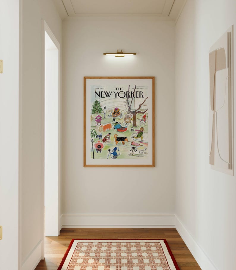 May include: A hallway with a framed "The New Yorker" magazine cover featuring a park scene with people and dogs. A red and white patterned rug sits on the wooden floor. A brass light fixture is above the artwork.