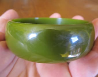 May include: A green plastic bangle bracelet. The bracelet is smooth and shiny.