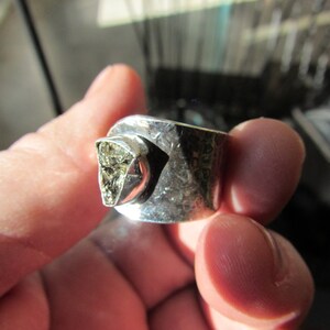 May include: A silver ring with a hammered finish and a large, irregular, light brown gemstone set in the center.
