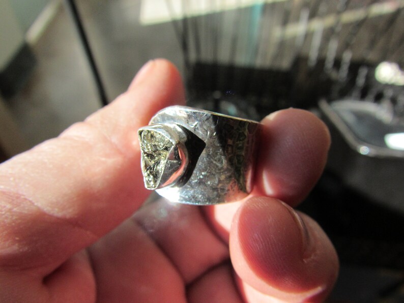 May include: A silver ring with a hammered finish and a large, irregular, light brown gemstone set in the center.