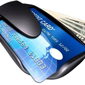 May include: A black wallet with a built-in money clip and a credit card holder. The credit card has the text "CREDIT CARD" and the date "01/98 THRU 12/02". The wallet is holding a stack of cash.