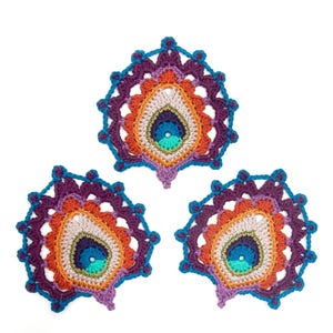 Pode incluir: Três desenhos de penas de pavão em crochê em tons de roxo, laranja, turquesa e verde. Os desenhos são intrincados e detalhados, com uma forma de lágrima central cercada por um padrão circular.