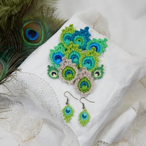 May include: Crocheted peacock feather earrings in shades of green, blue, and beige. The earrings are hanging from silver hooks.