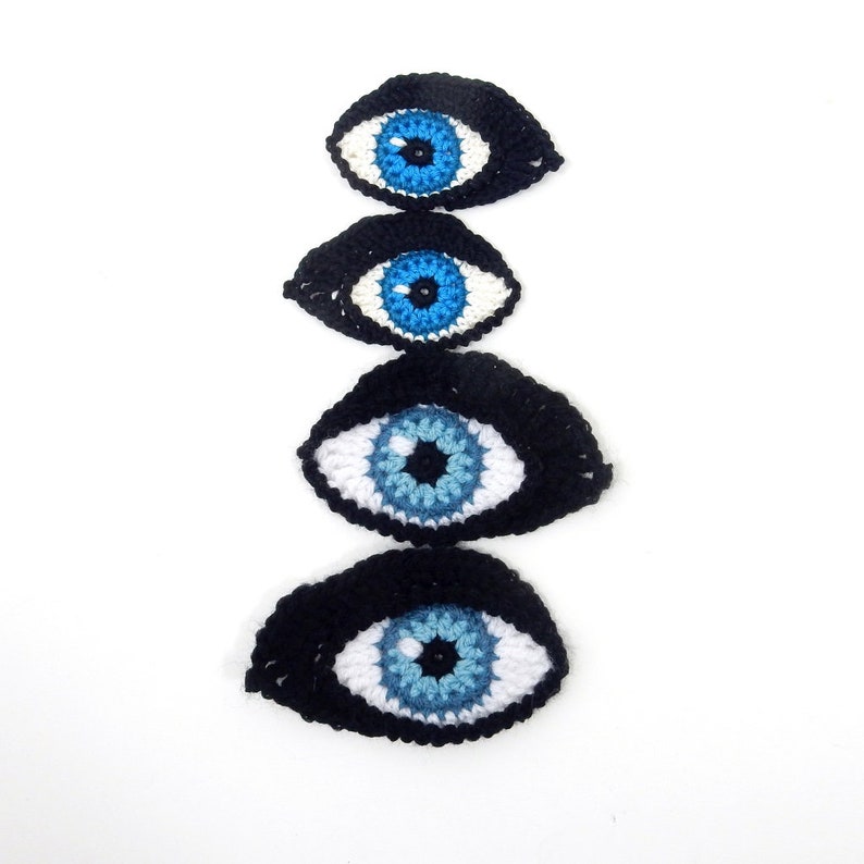 May include: Four crocheted evil eyes in different sizes, stacked on top of each other. The eyes are black with white and blue details.