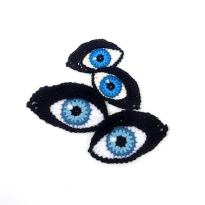 May include: Four crocheted evil eyes in black, white, and blue. The eyes are arranged in a stack, with the largest eye at the bottom and the smallest eye at the top.