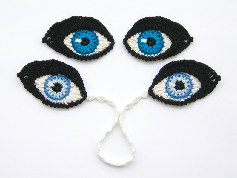 May include: Four crocheted eyes with black pupils and blue irises. The eyes are connected by a white crocheted string.