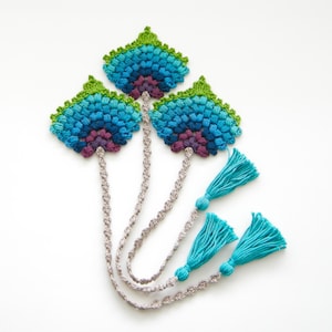 Op de afbeelding: Drie gehaakte bladwijzers met blauwe, groene en paarse ombre-ontwerpen en turquoise kwastjes.