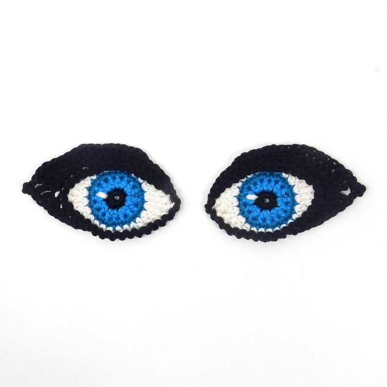 May include: Two crocheted eyes with black eyelashes, white irises, and blue pupils.