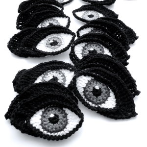 May include: A collection of crocheted black eye patches with white and gray irises. The eye patches are arranged in a staggered pattern, creating a visually appealing and unique design.