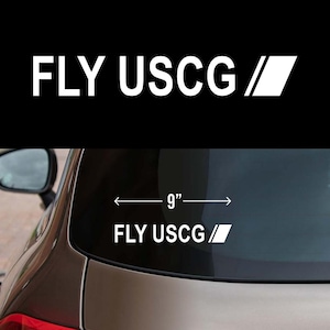 May include: A black car with a white vinyl decal on the back window. The decal says "FLY USCG /" and has a white arrow pointing to the right. The decal is 9 inches wide.
