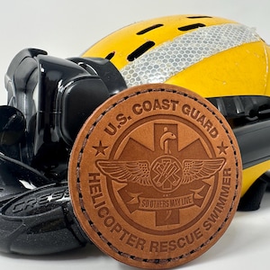 May include: A brown leather patch with the words "U.S. Coast Guard Helicopter Rescue Swimmer" and a logo with a winged medical cross and the words "So Others May Live".