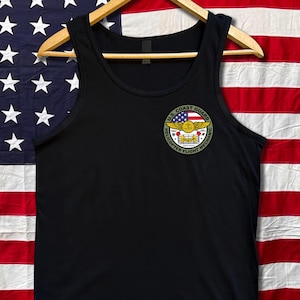 May include: Black tank top with a U.S. Coast Guard Helicopter Flight Mechanic patch on the chest. The patch features a design with a blue and white star field, red and white stripes, and the text "U.S. Coast Guard Helicopter Flight Mechanic".