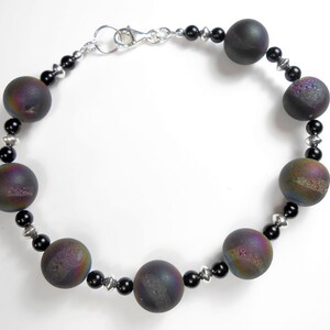 May include: A black and iridescent gemstone bracelet with a silver clasp. The bracelet features round beads with a textured surface.