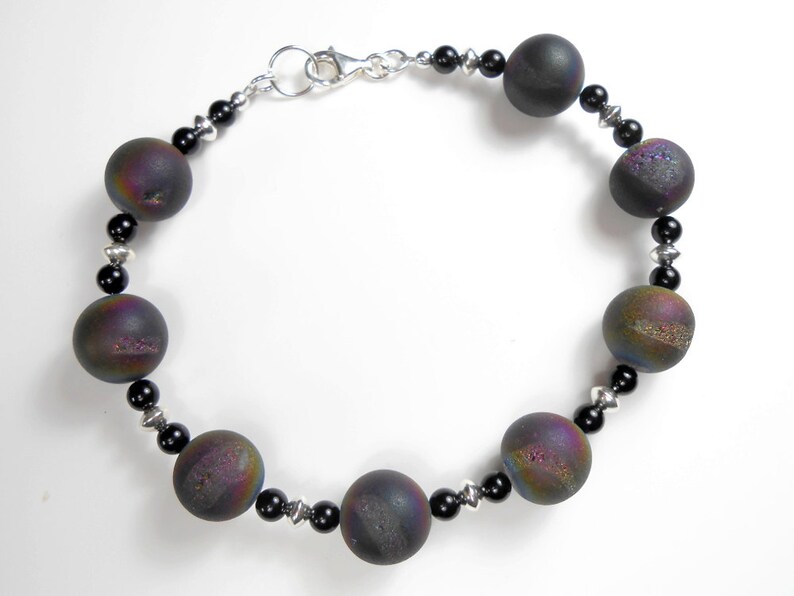 May include: A black and iridescent gemstone bracelet with a silver clasp. The bracelet features round beads with a textured surface.