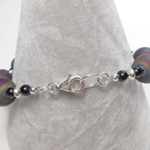May include: A silver chain bracelet with black and iridescent beads. The bracelet has a lobster clasp closure.