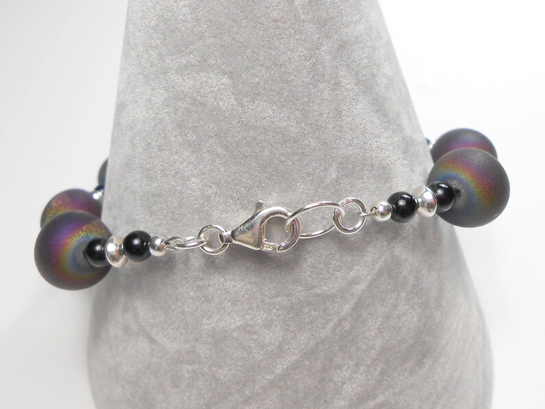 May include: A silver chain bracelet with black and iridescent beads. The bracelet has a lobster clasp closure.