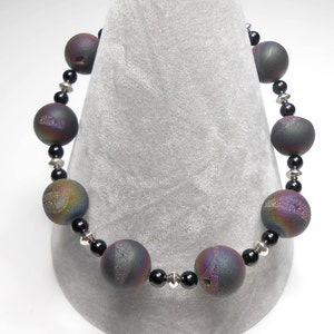 May include: A black and iridescent agate gemstone bracelet with silver spacer beads. The bracelet is made with round beads and is approximately 7 inches in length.