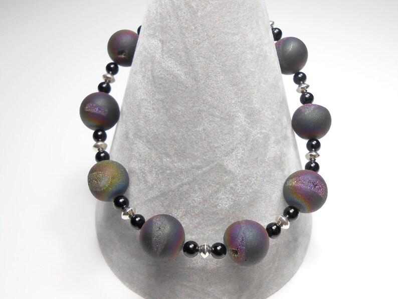May include: A black and iridescent agate gemstone bracelet with silver spacer beads. The bracelet is made with round beads and is approximately 7 inches in length.