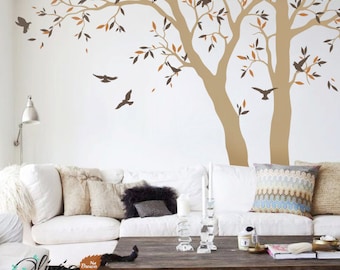 May include: A wall decal featuring two trees with brown branches and leaves in shades of brown and orange. The trees are silhouetted against a white wall. There are also small birds flying around the trees. The decal is perfect for adding a touch of nature to any room.